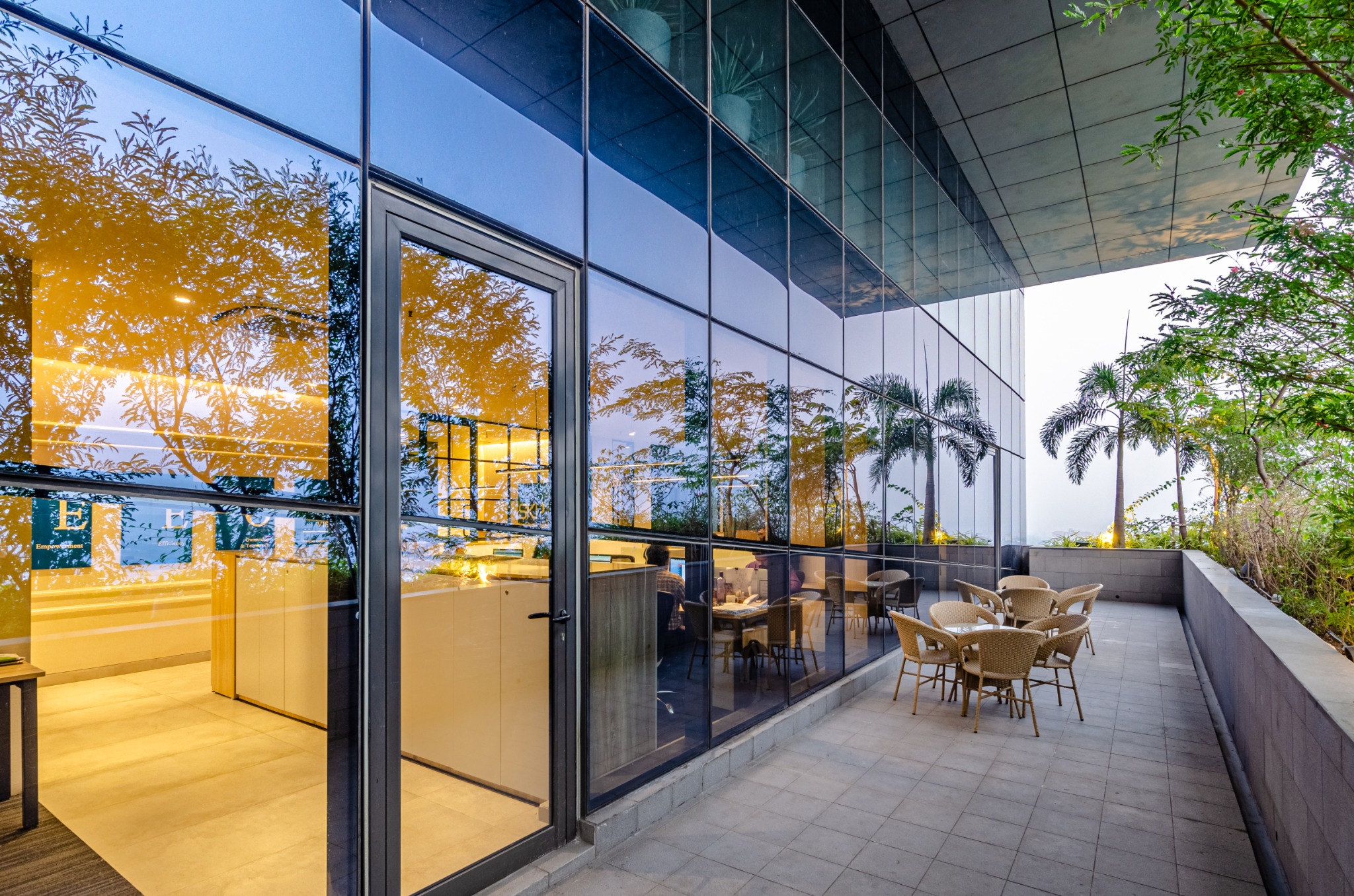 Glazed lounge opening onto a planted outdoor seating terrace at Biowonder, Kolkata